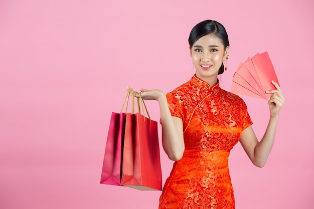 Sonrisa feliz hermosa mujer asiática y compras en año nuevo chino sobre fondo rosa.