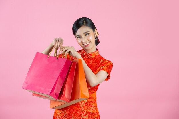 Sonrisa feliz hermosa mujer asiática y compras en año nuevo chino sobre fondo rosa.