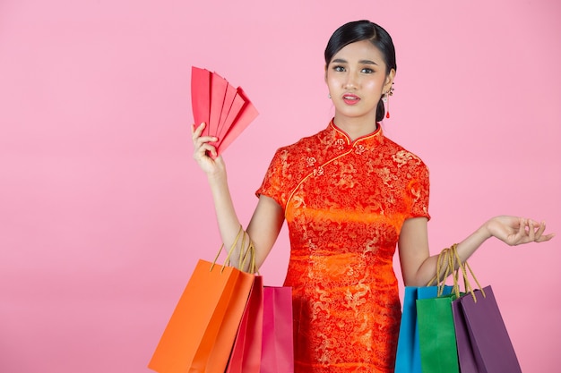 Sonrisa feliz hermosa mujer asiática y compras en año nuevo chino sobre fondo rosa.