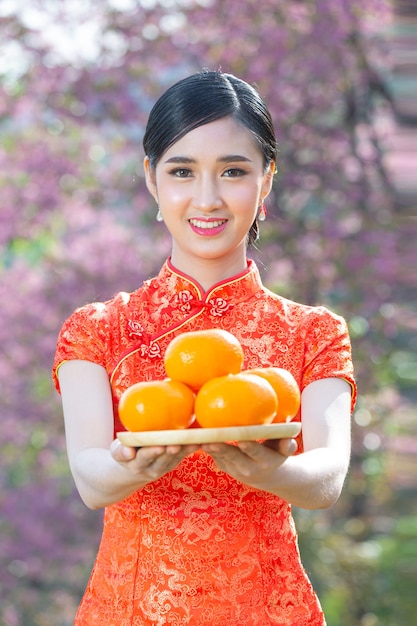 Sonrisa feliz hermosa mujer asiática y sosteniendo naranjas frescas en año nuevo chino sobre fondo rosa.