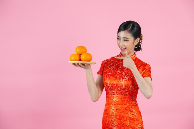 Sonrisa feliz hermosa mujer asiática y sosteniendo naranjas frescas en año nuevo chino sobre fondo rosa.