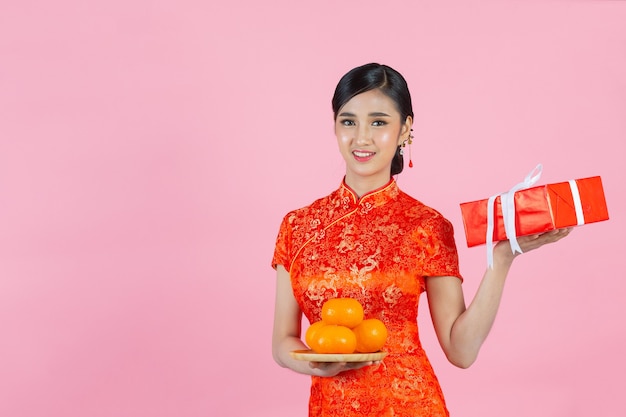 Sonrisa feliz hermosa mujer asiática y sosteniendo naranjas frescas en año nuevo chino sobre fondo rosa.