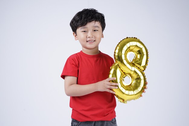 Sonrisa feliz del muchacho del niño pequeño asiático con el globo del número de la hoja, aislado en el fondo blanco