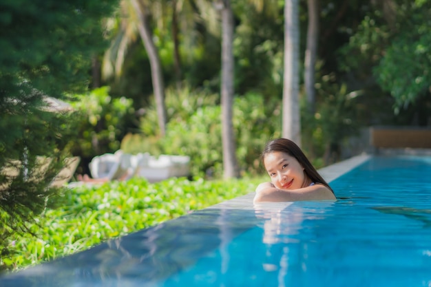 Sonrisa feliz de la mujer asiática joven hermosa del retrato en piscina alrededor del centro turístico y del hotel