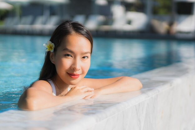 Sonrisa feliz de la mujer asiática joven hermosa del retrato en piscina alrededor del centro turístico y del hotel