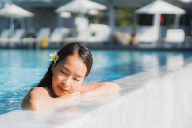 Sonrisa feliz de la mujer asiática joven hermosa del retrato en piscina alrededor del centro turístico y del hotel