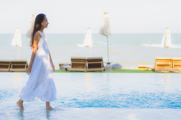 Foto gratuita la sonrisa feliz de la mujer asiática joven hermosa del retrato y se relaja alrededor de piscina en centro turístico del hotel