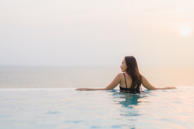 La sonrisa feliz de la mujer asiática joven hermosa del retrato se relaja alrededor de piscina en centro turístico del hotel