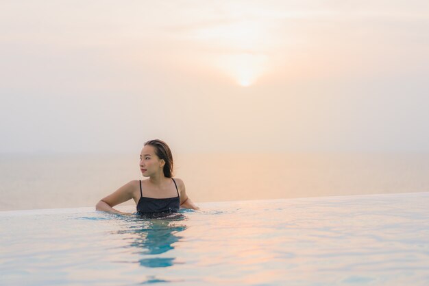 La sonrisa feliz de la mujer asiática joven hermosa del retrato se relaja alrededor de piscina en centro turístico del hotel