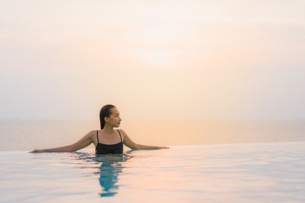 La sonrisa feliz de la mujer asiática joven hermosa del retrato se relaja alrededor de piscina en centro turístico del hotel