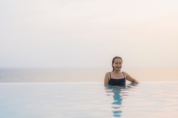 La sonrisa feliz de la mujer asiática joven hermosa del retrato se relaja alrededor de piscina en centro turístico del hotel