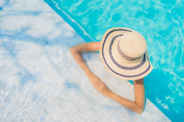 La sonrisa feliz de la mujer asiática joven hermosa del retrato se relaja en la piscina para las vacaciones del viaje