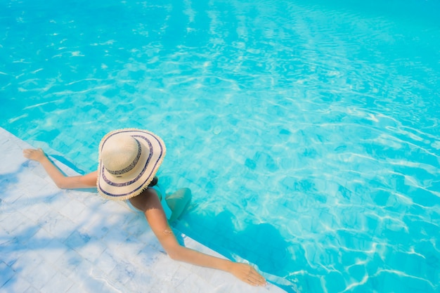 La sonrisa feliz de la mujer asiática joven hermosa del retrato se relaja en la piscina para las vacaciones del viaje