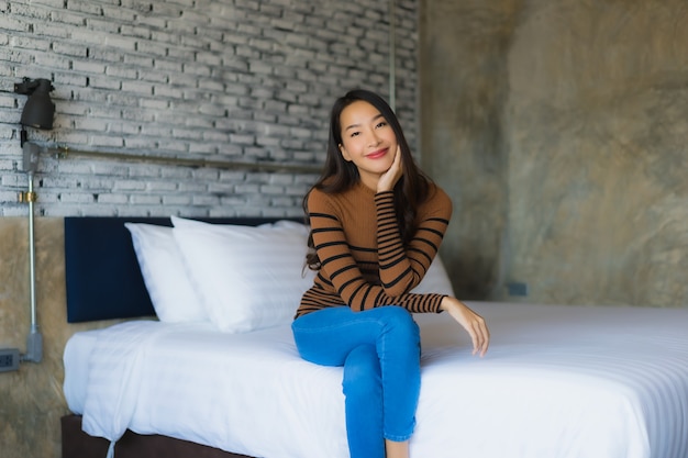 La sonrisa feliz de la mujer asiática joven se relaja en cama en dormitorio