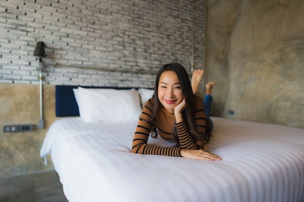 La sonrisa feliz de la mujer asiática joven se relaja en cama en dormitorio