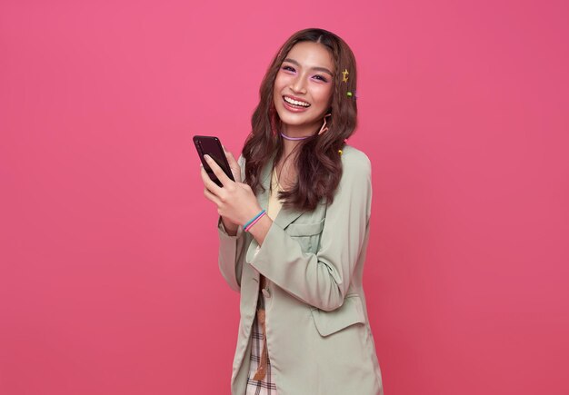 Sonrisa feliz mujer asiática a través de teléfono móvil aislado sobre fondo de color rosa