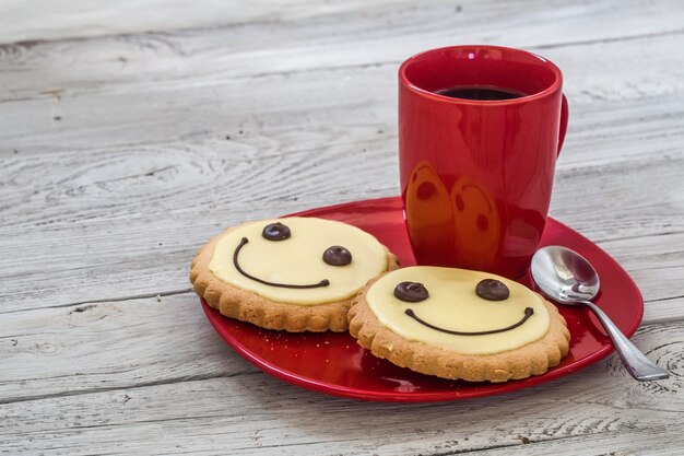 Sonrisa galletas en una placa roja con taza de café, pared de madera, comida