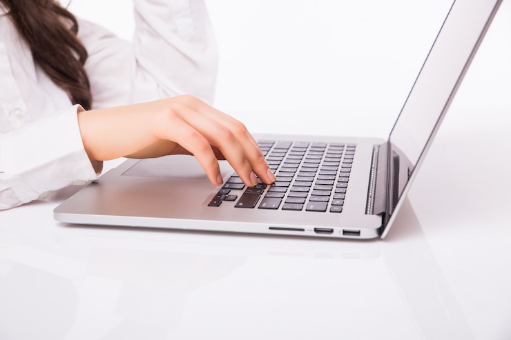 Foto gratuito sonrisa hermosa de la mujer de negocios que se sienta en el escritorio que trabaja usando la computadora portátil que mira la pantalla, escritura a mano, aislada sobre la pared blanca