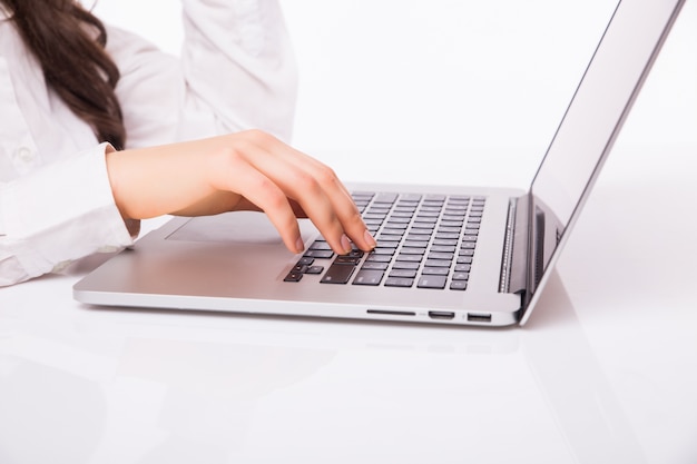 Sonrisa hermosa de la mujer de negocios que se sienta en el escritorio que trabaja usando la computadora portátil que mira la pantalla, escritura a mano, aislada sobre la pared blanca