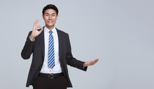 Sonrisa de hombre de negocios asiático de rostro guapo y amigable en gesto de traje formal o mostrando la mano ok