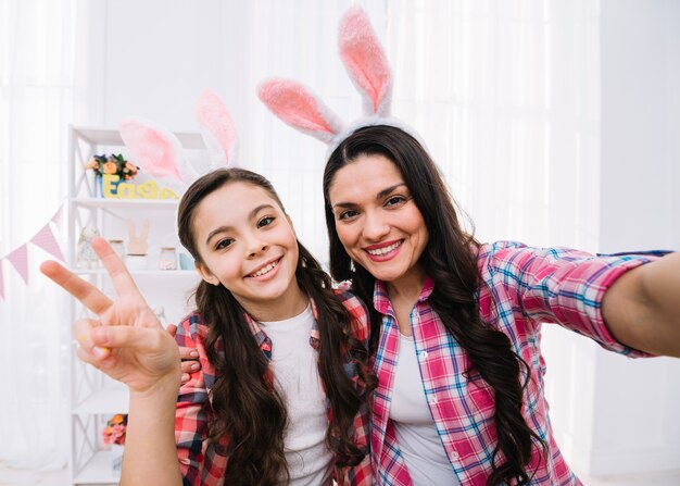 Sonrisa madre e hija con orejas de conejo mostrando el signo de paz