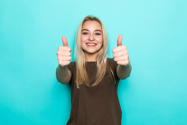 Sonrisa mujer bastante joven que muestra los pulgares para arriba aislados en la pared azul