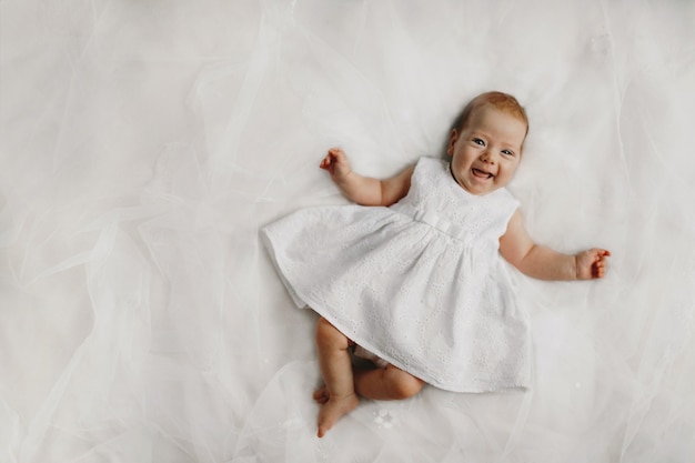 Sonrisa sincera de la pequeña niña vestida con un vestido blanco en la cama