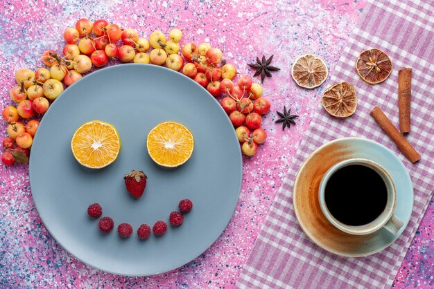 Sonrisa de vista superior de frutas dentro del plato con frutas frescas y té en el escritorio de color rosa brillante