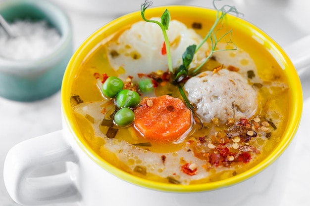 Sopa con albóndigas, coliflor, guisantes, zanahorias y crema sobre un fondo blanco.