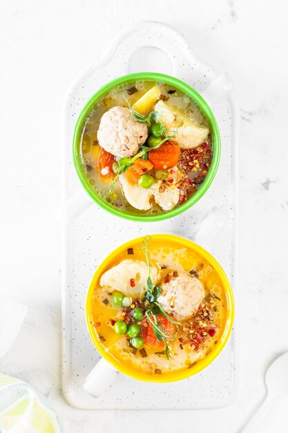 Sopa con albóndigas de pollo y verduras de primavera sobre un fondo blanco Vertical