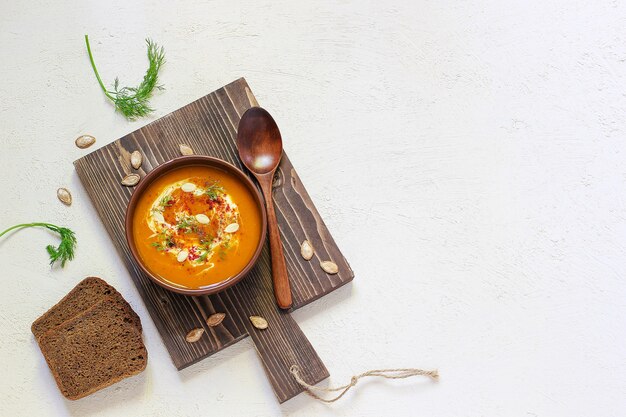 Sopa asada de calabaza y zanahoria con crema, pimienta negra y semillas de calabaza, tabla de cortar y rodajas de calabaza fresca, pan negro