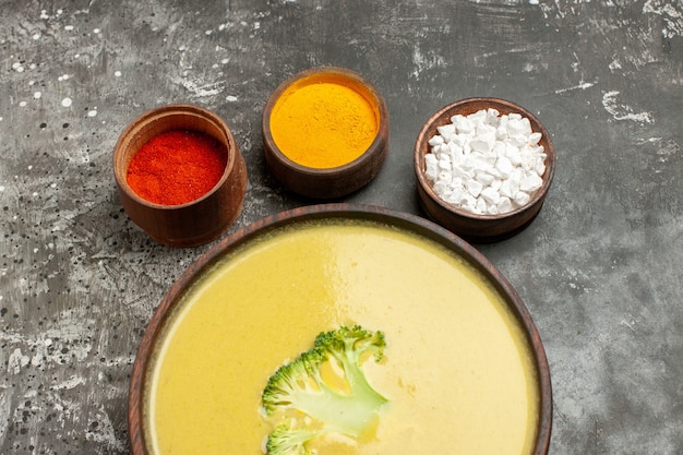 Sopa de brócoli en un recipiente marrón y diferentes especias en mesa gris