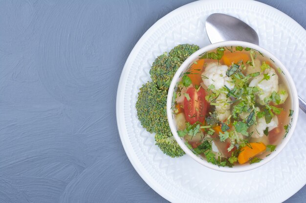 Sopa de brócoli con verduras y hierbas en una taza blanca.