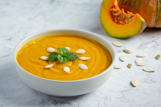 Sopa de calabaza en un tazón blanco colocado sobre un piso de mármol blanco