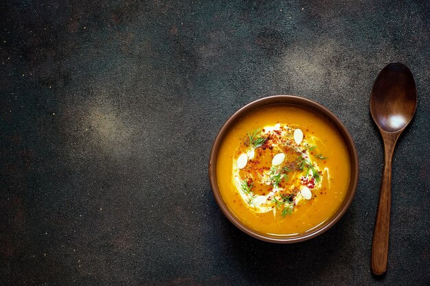 Sopa de calabaza y zanahoria asada con crema, semillas y verde fresco en un tazón de cerámica. Vista superior