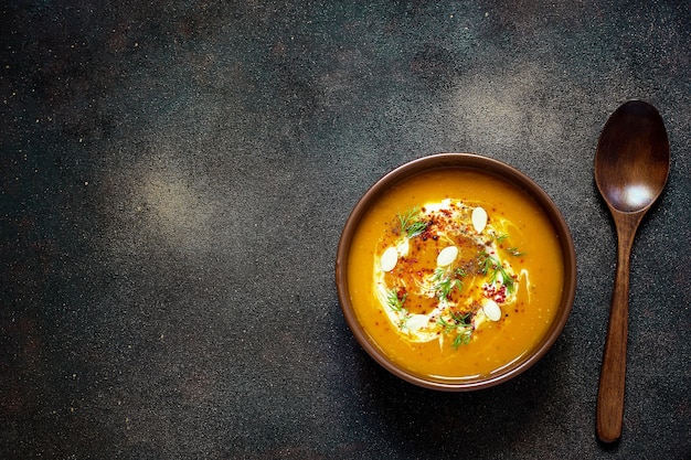 Sopa de calabaza y zanahoria asada con crema, semillas y verde fresco en un tazón de cerámica. Vista superior