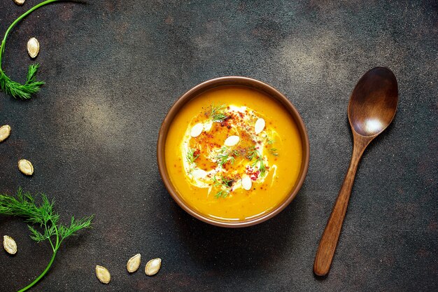 Sopa de calabaza y zanahoria asada con crema, semillas y verde fresco en un tazón de cerámica. Vista superior