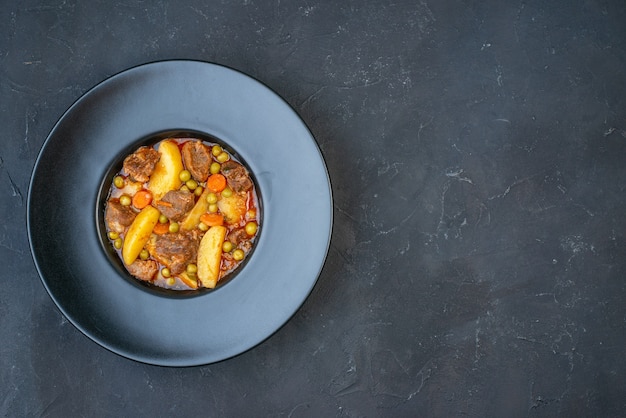 Sopa de carne de vista superior con guarnición en placa negra sobre mesa oscura con lugar libre