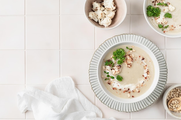 Sopa de crema de coliflor con nueces de pino en un cuenco sobre un fondo blanco