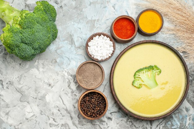 Sopa cremosa de brócoli en un tazón marrón diferentes especias y brócoli fresco en mesa gris