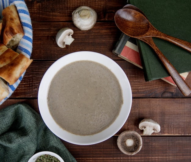 Sopa cremosa de champiñones dentro de un tazón blanco servido con pan, vire superior