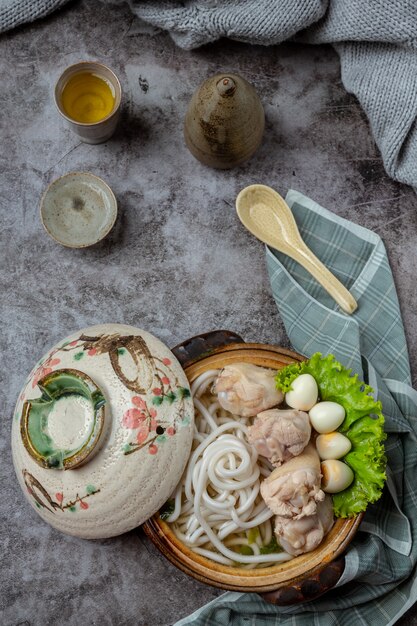 Sopa de estilo asiático con fideos, carne de cerdo y cebolla verde de cerca en un recipiente sobre la mesa.