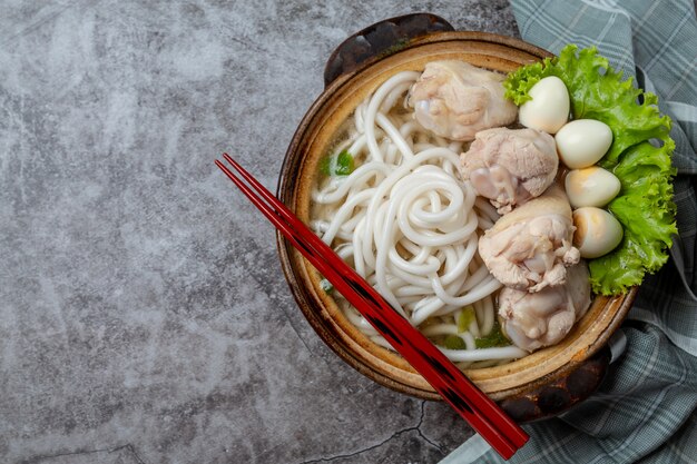 Sopa de estilo asiático con fideos, carne de cerdo y cebolla verde de cerca en un recipiente sobre la mesa.