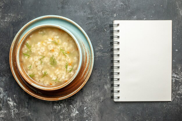 Sopa de estrella vista superior en un tazón un cuaderno sobre una superficie oscura