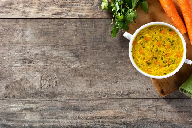 Sopa de fideos con pollo en un tazón blanco sobre mesa de madera