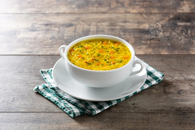 Sopa de fideos con pollo en un tazón blanco sobre mesa de madera