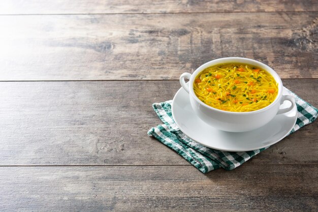 Sopa de fideos con pollo en un tazón blanco sobre mesa de madera