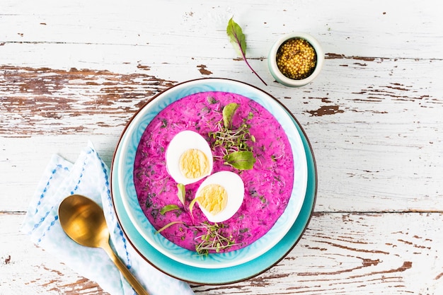 Foto gratuita sopa fría hecha de remolacha, pepinos y adornada con un huevo en un plato azul sobre un fondo de madera vista superior espacio de copia