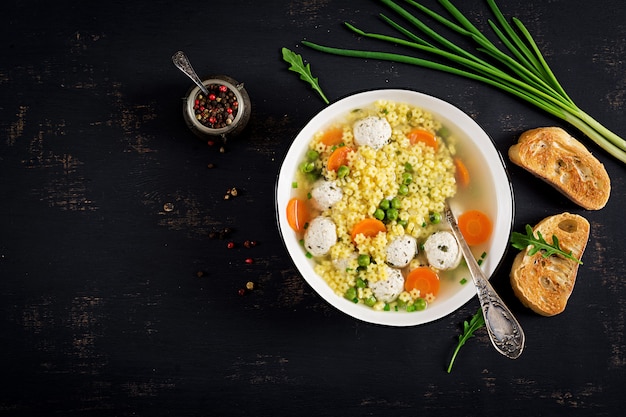 Sopa italiana de albóndigas y pasta sin gluten Stelline en un tazón sobre la mesa negra.