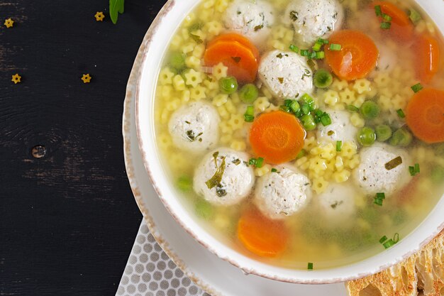 Sopa italiana de albóndigas y pasta Stelline en un tazón sobre mesa negra